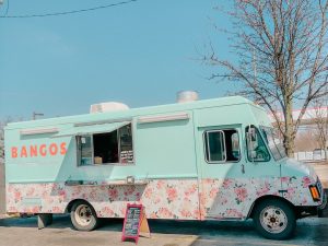 Picture of a blue food truck with a floral design on the bottom. Text on truck reads Bangos.