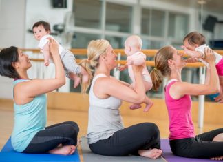 3 women holding their babies near their faces while sitting on yoga mats.