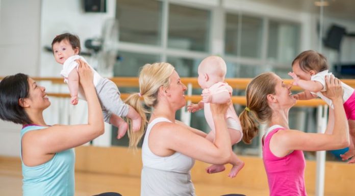 3 women holding their babies near their faces while sitting on yoga mats.